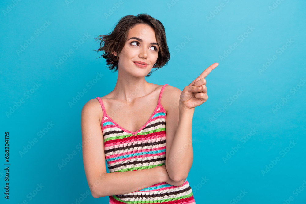 Photo of dreamy shiny woman dressed striped tank top showing finger empty space isolated blue color background Photo of dreamy shiny woman dressed striped tank top showing finger empty space isolated blue color background