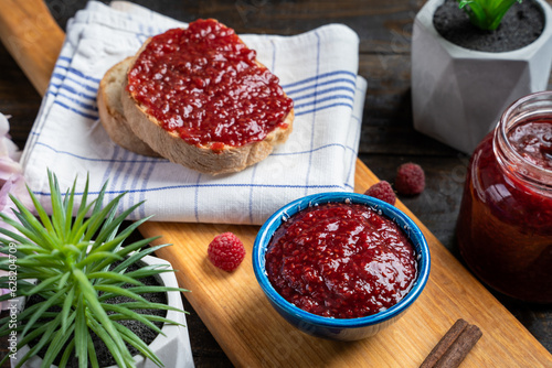 Fresh homemade raspberry jam in a bowl served on a wooden platter with bread