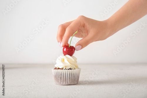 Slika na platnu Woman decorating tasty cupcake with cherry on light background