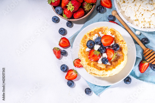 Sweet homemade cottage cheese pancakes, american version of syrniki or cottage cheese fritters, big pan fried cheesy pancakes with fresh summer blueberry and strawberry, healthy high-protein breakfast