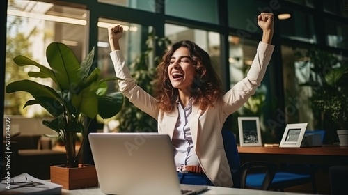  Joyful business woman freelancer entrepreneur smiling and rejoices in victory while sitting at desk and working at laptop after finishing project in home office.