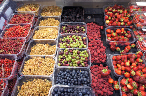 Ripe berries in containers in the market. Strawberries, raspberries, currants, blueberries, gooseberries, blackberries in the store counter.