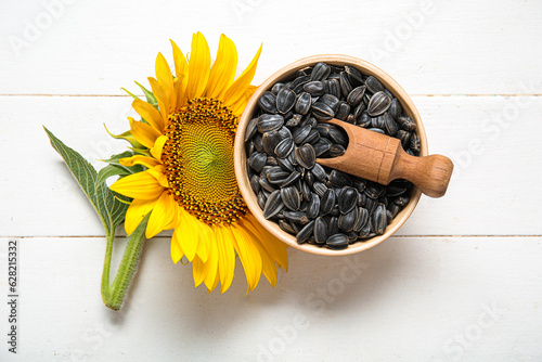 Beautiful sunflower and bowl with seeds on white wooden background