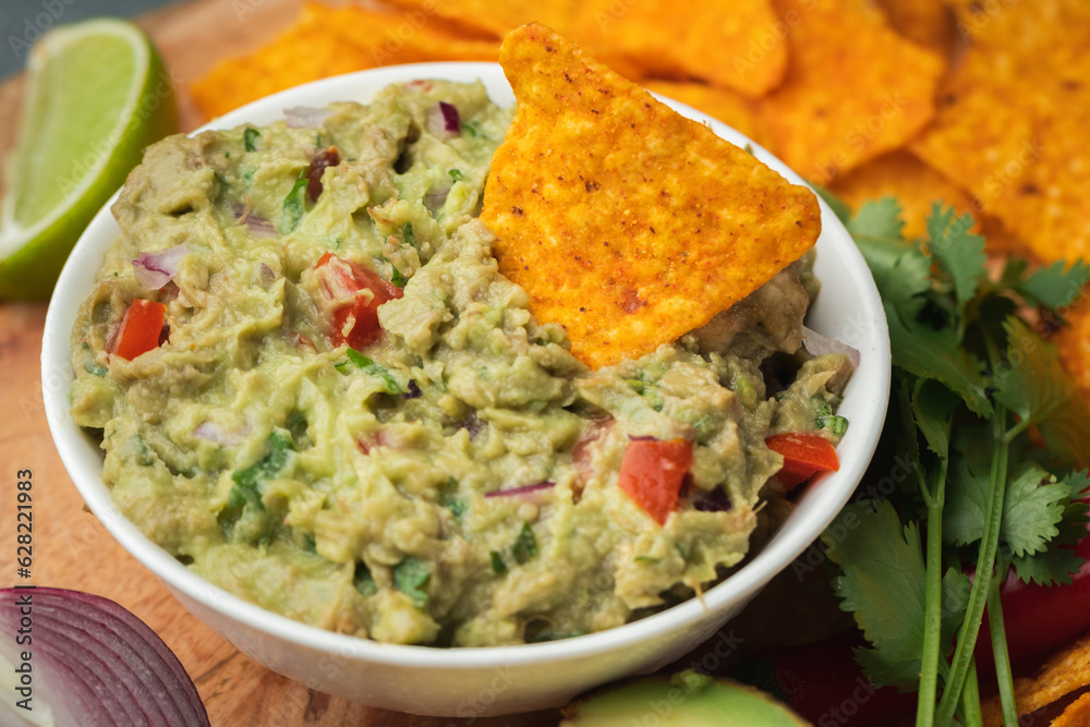 White bowl of traditional Mexican guacamole with nachos on grey concrete background. Tortilla chips with guacamole sauce dip and ingredients: avocado, cilantro, onion, hot pepper and lime White bowl of traditional Mexican guacamole with nachos on grey concrete background. Tortilla chips with guacamole sauce dip and ingredients: avocado, cilantro, onion, hot pepper and lime