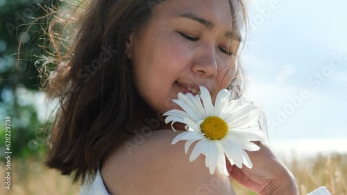 Happy woman with big chamomile in her hand in summer field. Carefree girl enjoys freedom and tranquility in the countryside during her vacation. The concept of rest or relaxation and happiness or photo