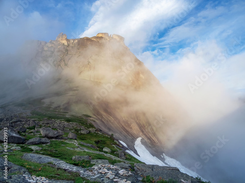 Soft focus. Sunrise in the mountains, in thick clouds. Light on the pass. The glacier is melting, illuminated by the bright golden morning sun.