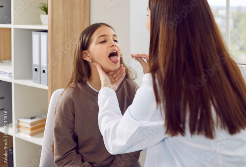 Back view of doctor otolaryngologist examining teenage girl patient's throat in medical office during checkup. Doctor woman pediatrician exam the oral cavity of a sick child in examination room. photo