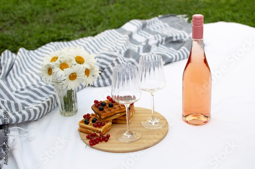 Romantic, summer picnic in park on the grass. Champagne and two glasses on white plaid. Concept of food and drink.