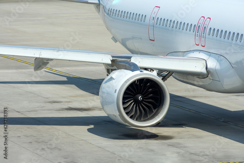 View of the engine of a passenger jet aircraft wing and fuselage with portholes on the platform parking.