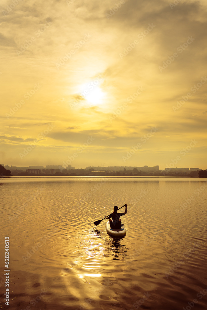 Stand up kayaking or stand-up paddleboarding on a quiet lake at sunset during a warm summer beach holiday, active woman. Stand up kayaking or stand-up paddleboarding on a quiet lake at sunset during a warm summer beach holiday, active woman.