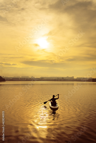 Stand up kayaking or stand-up paddleboarding on a quiet lake at sunset during a warm summer beach holiday, active woman.