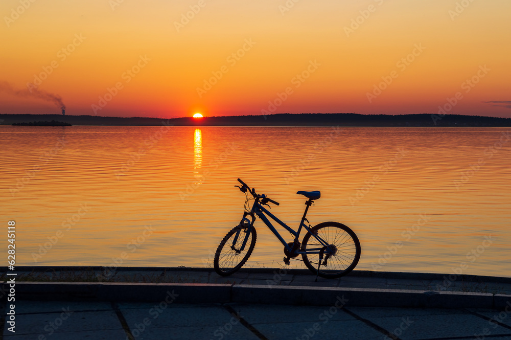 Fototapeta premium Landscape with a bicycle on the shore of the lake at sunset