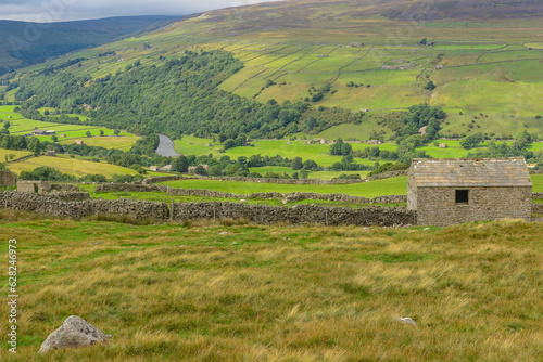 The beautiful, rural Yorkshire Dales in Summer time as seen from the High Road, Gunnerside in Swaledale, with stone barns, the River Swale, pastures and dry stone walling.  Horizontal.  Copy Space photo