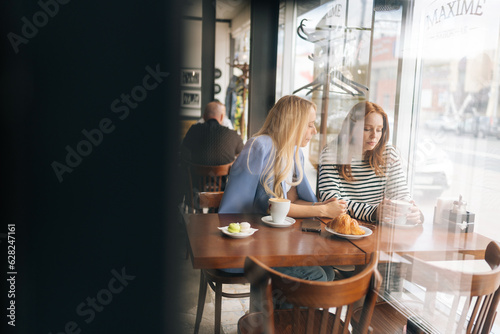 View from door glass to upset young woman telling best friend about boyfriend betrayal. Compassion showed to real best girlfriends. Life problem concept. Gossiping along with friend at coffee shop.