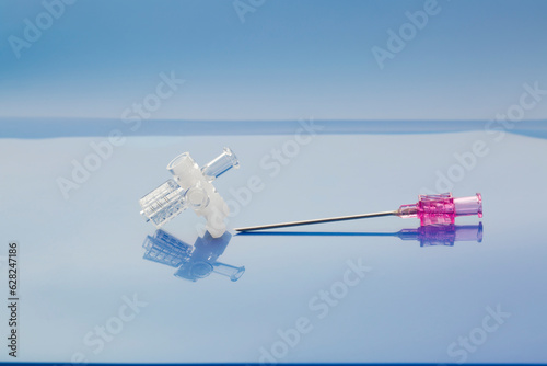 Medical devices used during diagnosis and drainage of liquid and gas accumulation in the pleural cavity. Three-way stopcock and percutaneous entry needle on light blue background