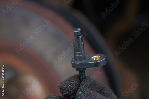 Worker hold in hand new ABS sensor, replace damaged electrical sensor. Technician hand holding small antilock brake system spare part. ABS brake sensor replacement work. Selective focus. photo
