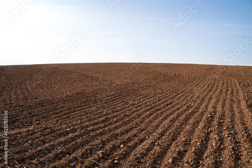 Tela Plowed farmland with brown soil and a blue sunny sky