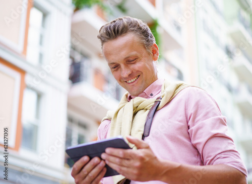 Happy man reading latest news articles from tablet PC while being outdoors on city street. Tablet PC in his hands allows him to access the latest information and stay up-to-date with current events. 