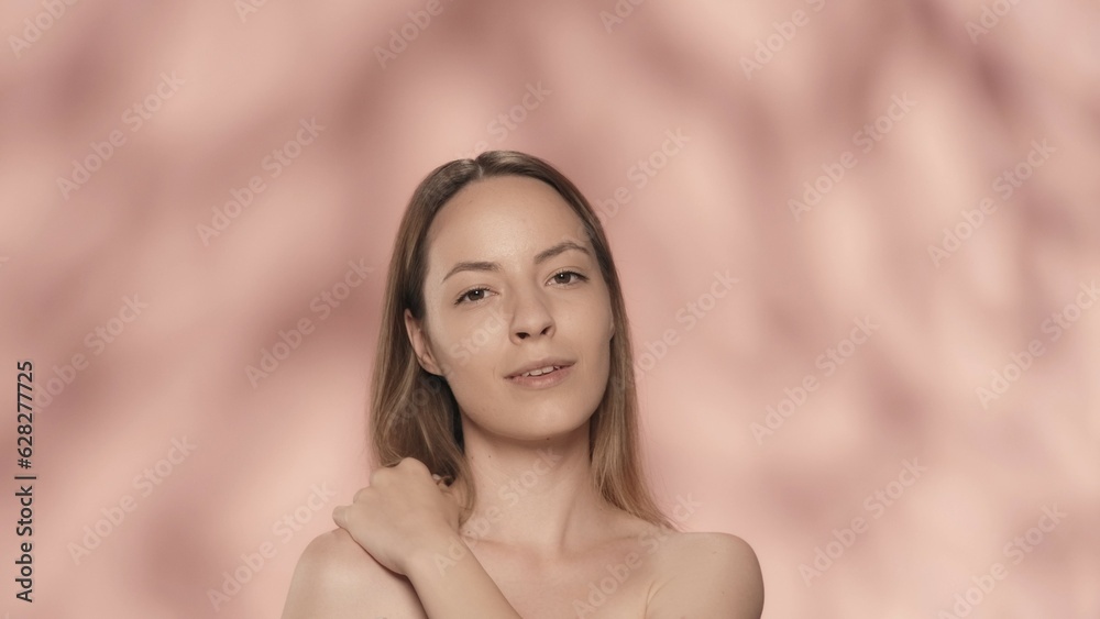 Obraz premium A young woman enjoys her perfect smooth, delicate skin. Portrait of a smiling seminude woman, isolated on a pink background close up. The concept of beauty, cosmetology, skin care, spa.
