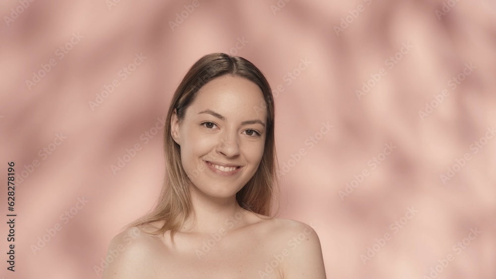 Portrait of a smiling seminude woman on a pink background close up. A woman with natural makeup looks straight ahead. Beauty concept. Natural beauty, cosmetology, skin care. Portrait of a smiling seminude woman on a pink background close up. A woman with natural makeup looks straight ahead. Beauty concept. Natural beauty, cosmetology, skin care.