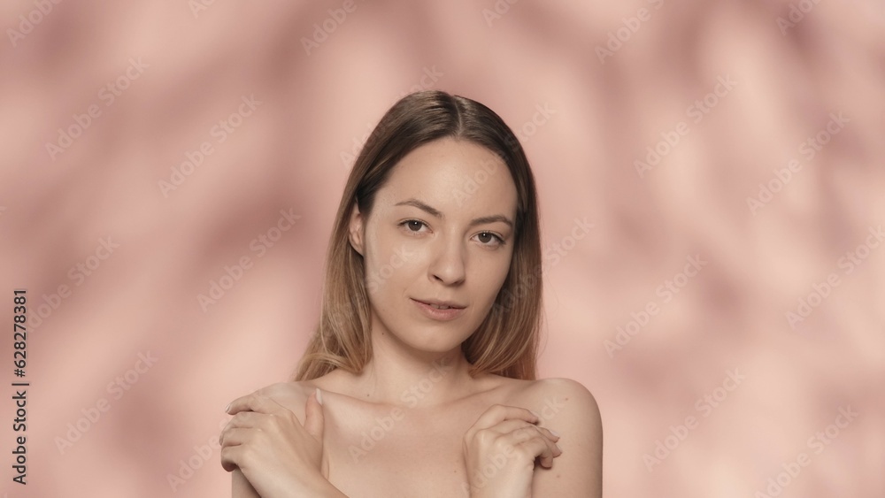 The woman crosses her arms and touches the bare skin of her shoulders. Portrait of an attractive seminude woman in the studio on a pink background close up. The concept of beauty, cosmetology and care The woman crosses her arms and touches the bare skin of her shoulders. Portrait of an attractive seminude woman in the studio on a pink background close up. The concept of beauty, cosmetology and care