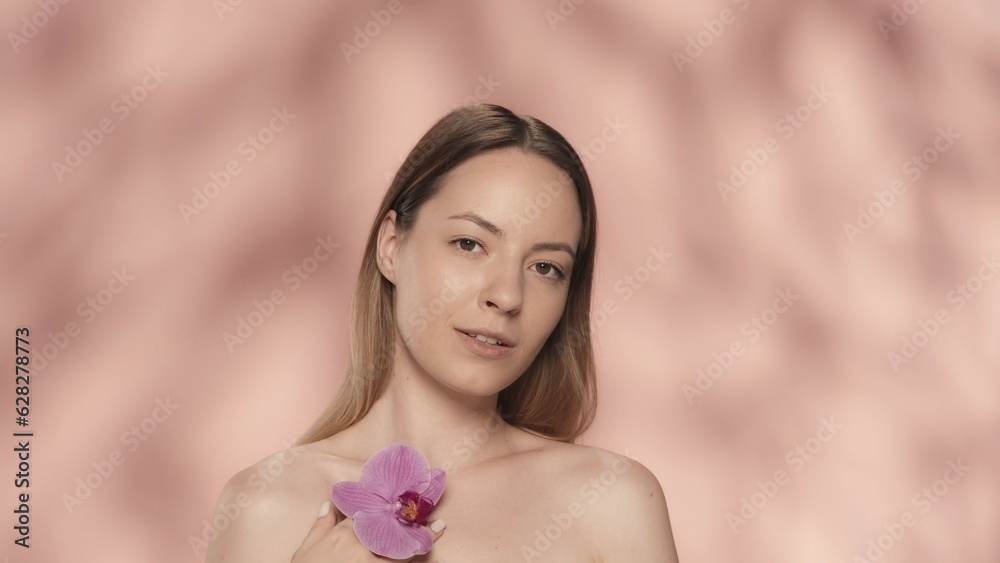 A woman touches an orchid flower to the clean, smooth skin. Portrait of a woman with an orchid flower in her hand in the studio on a pink background close up. A woman touches an orchid flower to the clean, smooth skin. Portrait of a woman with an orchid flower in her hand in the studio on a pink background close up.