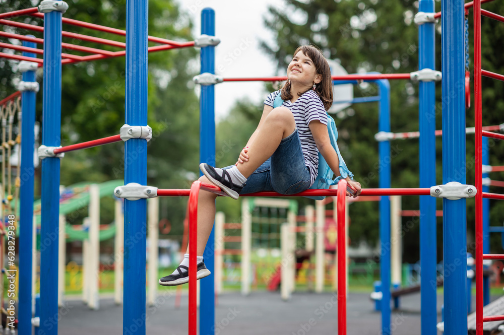Obraz premium back to school. happy smiling child girl 11 years old teenager with a backpack.stands on the background of the sports ground near the school. High quality photo