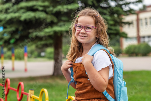 back to school. happy smiling girl 6 years old with a backpack. standing in front of a sports field near the school. High quality photo. 