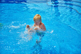 Young boy kid child eight years old splashing in swimming pool having fun leisure activity. Boy happy swimming in a pool. Activities on the pool, children swimming and playing in water, happiness and
