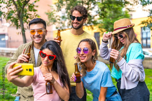 Multi ethnic group of friends partying in the city park taking a selfie, friendship and fun concept wearing sunglasses and drinking beer © unai