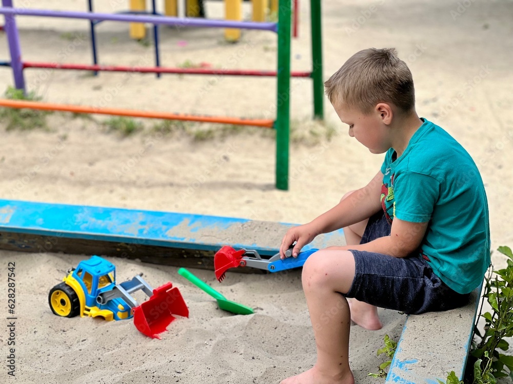 A little boy playing in the sandbox at the playground outdoors. Child playing with sand cars. Outdoor creative activities for kids. A little boy playing in the sandbox at the playground outdoors. Child playing with sand cars. Outdoor creative activities for kids.