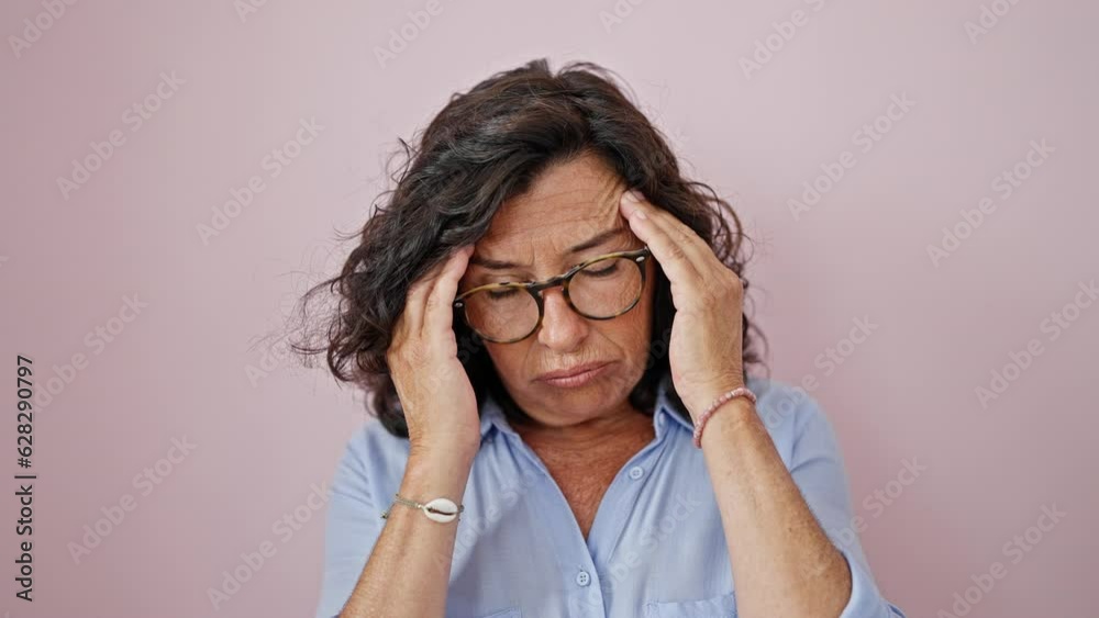 Middle age hispanic woman taking glasses off suffering for headache over isolated pink background Middle age hispanic woman taking glasses off suffering for headache over isolated pink background