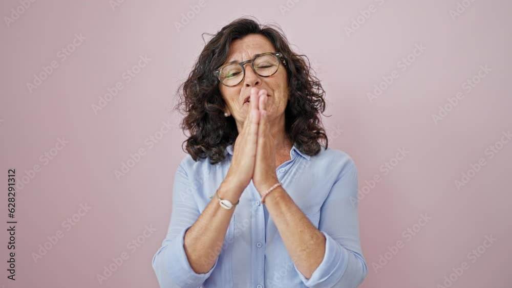 Middle age hispanic woman doing please gesture with hands together over isolated pink background