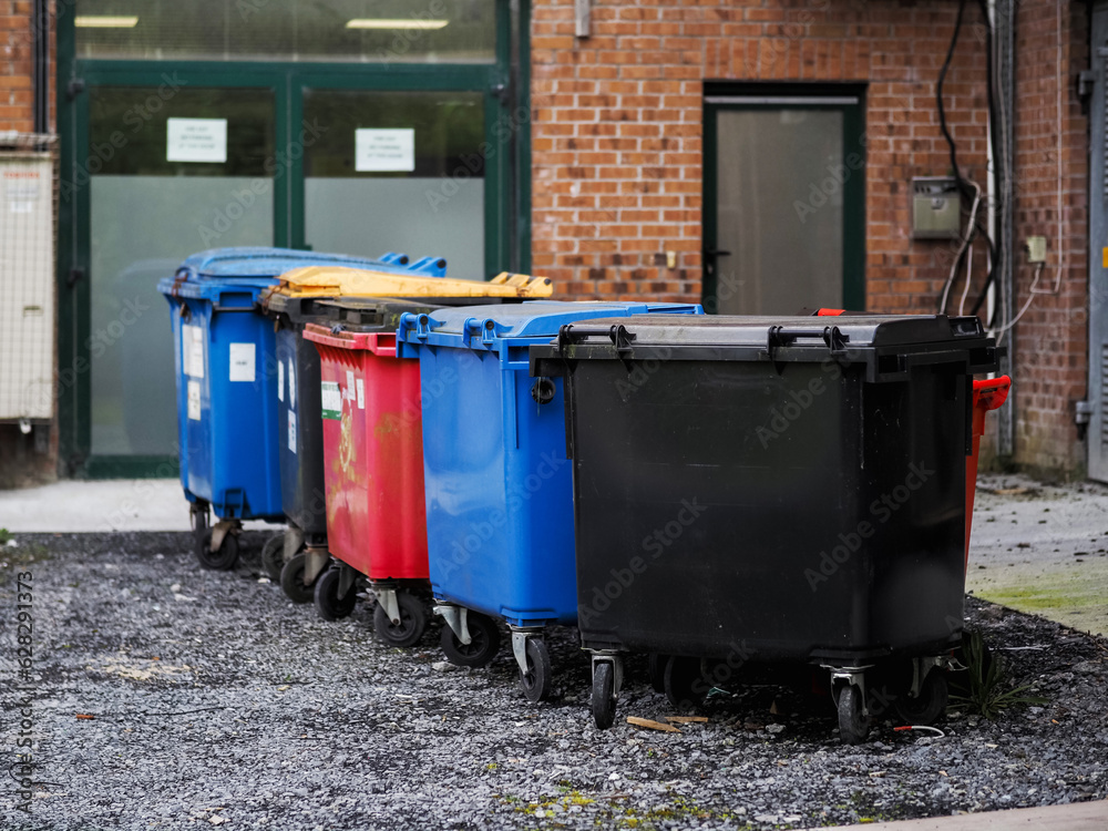 Back yard of an office building with colored rubbish bins, fire doors and utility room entrance. Many air conditioner units mounted on a brick wall. Dirt on the ground Back yard of an office building with colored rubbish bins, fire doors and utility room entrance. Many air conditioner units mounted on a brick wall. Dirt on the ground