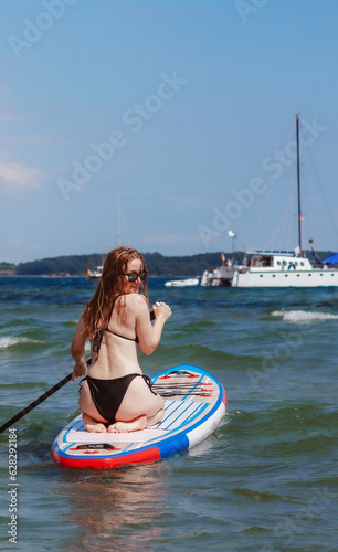 Back view of a woman riding stand up paddle board in the sea. Fun sport activity in the summer. © TatjanaMeininger