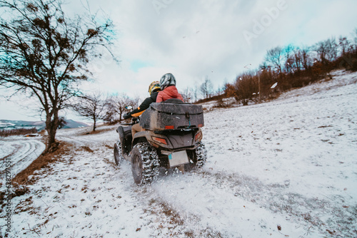 A young adventurous couple embraces the joy of love and thrill as they ride an ATV Quad through the snowy mountainous terrain © Minet