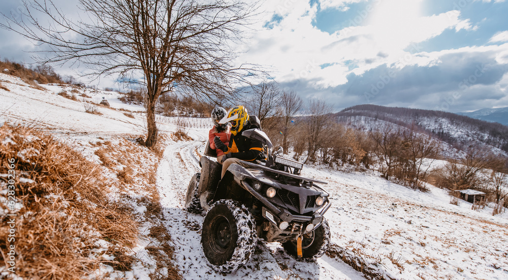 A young adventurous couple embraces the joy of love and thrill as they ride an ATV Quad through the snowy mountainous terrain A young adventurous couple embraces the joy of love and thrill as they ride an ATV Quad through the snowy mountainous terrain