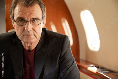 Portrait of mature business man wearing glasses sitting in seat aboard private jet  photo