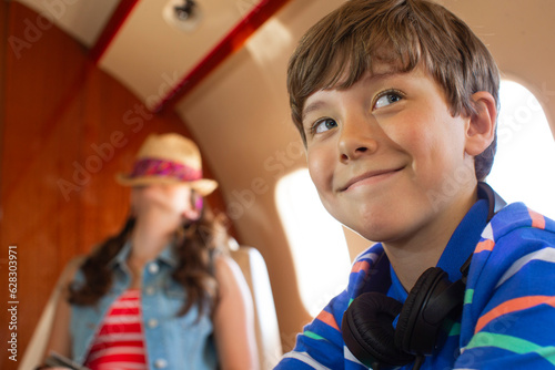 Siblings in cabin of private jet, brother smiling looking over shoulder sister asleep in background photo
