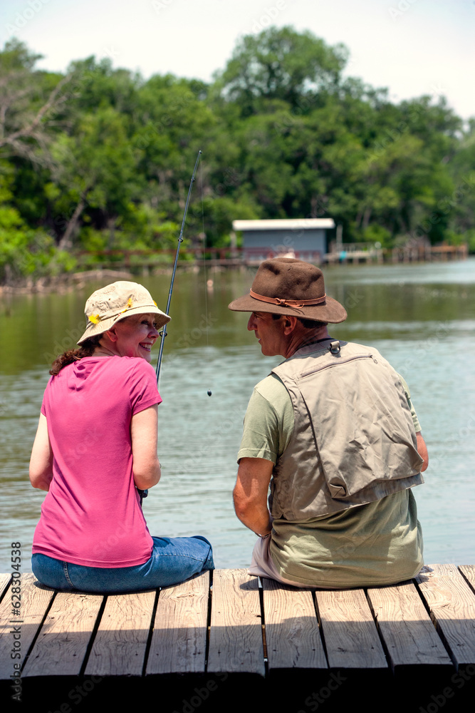 Woman with fishing line in the water sitting on edge of covered boat dock with husband Woman with fishing line in the water sitting on edge of covered boat dock with husband