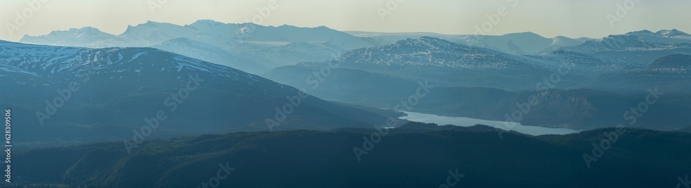 View over nordic mountain peaks in Norway from a hike up Hauknestinden, Hauknes, Mo i Rana, Helgeland, Norway. High peaks in a fjord landscape, snow covered. Clear Norwegian summer skies. Wild Norway View over nordic mountain peaks in Norway from a hike up Hauknestinden, Hauknes, Mo i Rana, Helgeland, Norway. High peaks in a fjord landscape, snow covered. Clear Norwegian summer skies. Wild Norway