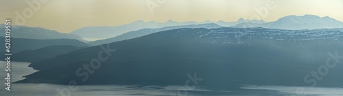 View over nordic mountain peaks in Norway from a hike up Hauknestinden, Hauknes, Mo i Rana, Helgeland, Norway. High peaks in a fjord landscape, snow covered. Clear Norwegian summer skies. Wild Norway	