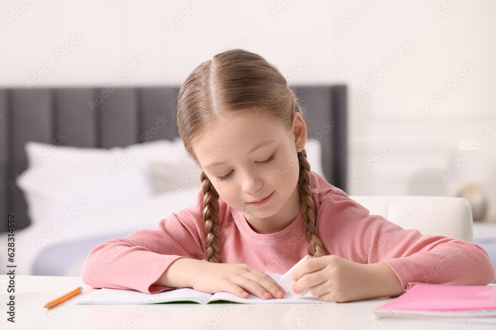 Girl using eraser at white desk in room Girl using eraser at white desk in room