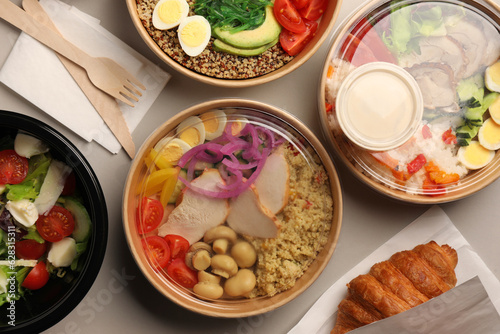 Tasty food in containers with wooden knife and fork on light grey table, flat lay