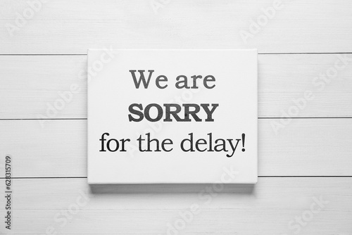 Canvas with phrase We Are Sorry For The Delay on white wooden background