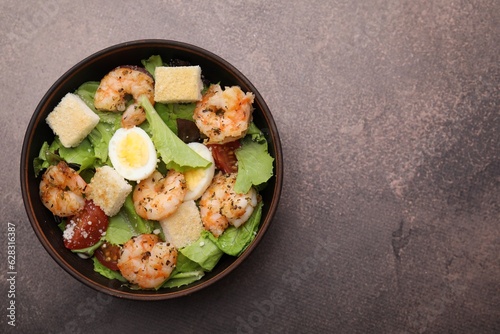 Delicious Caesar salad with shrimps on brown table, top view. Space for text