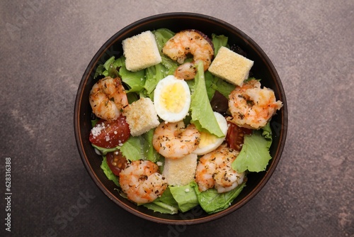 Delicious Caesar salad with shrimps on brown table, top view