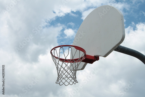 outdoor basketball net with white backboard and mesh screen right with silver post protruding from its back, clouds in background photo