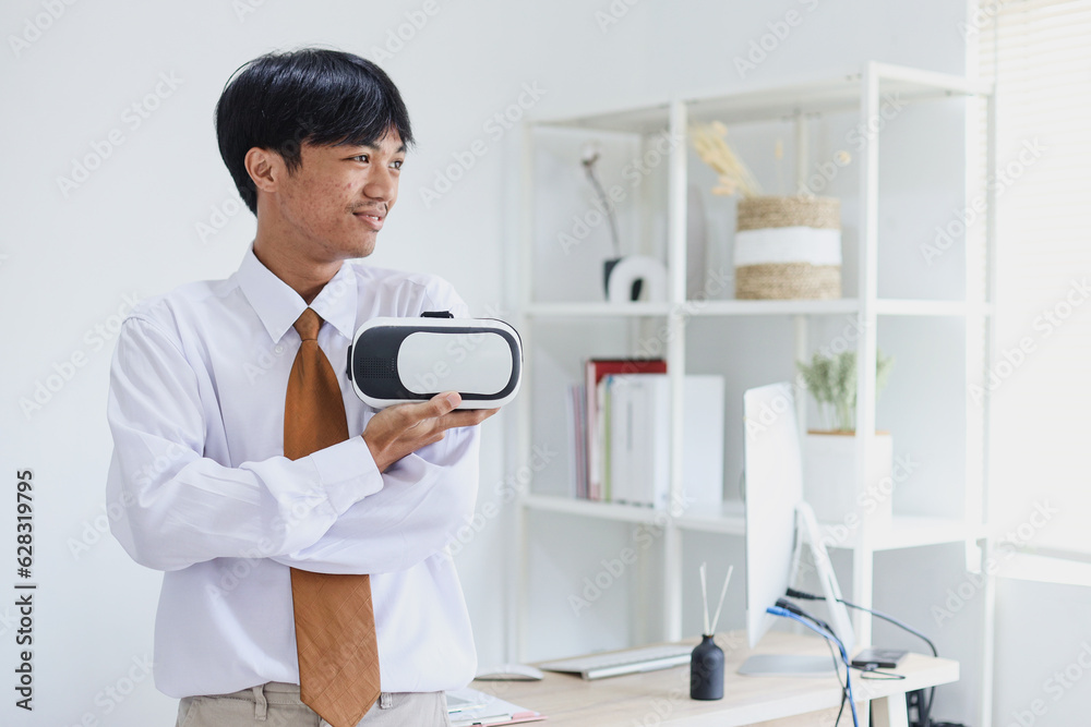 Happy young Asian man wearing formal clothes holding VR glasses on hand and looking away. Technology evolution and modern lifestyle