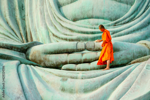 Cuadro en lienzo Young monk stay alone on green big buddha statue and clean in area of hands of statue with warm light of early morning